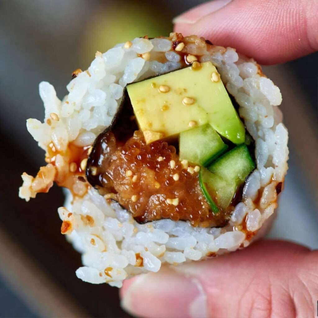 Messy sushi roll crumbling in thumb grip.