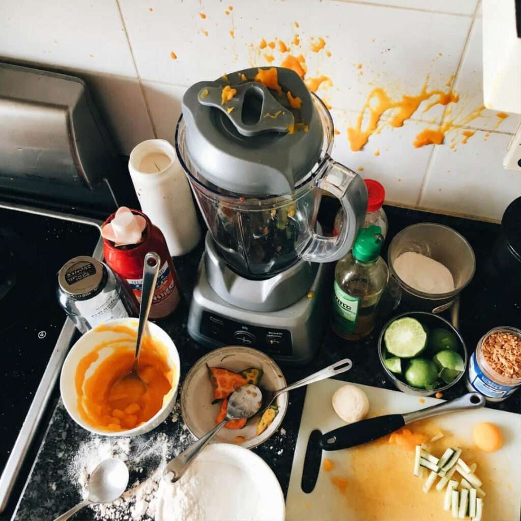 Cluttered counter with blender, mango splatters everywhere.