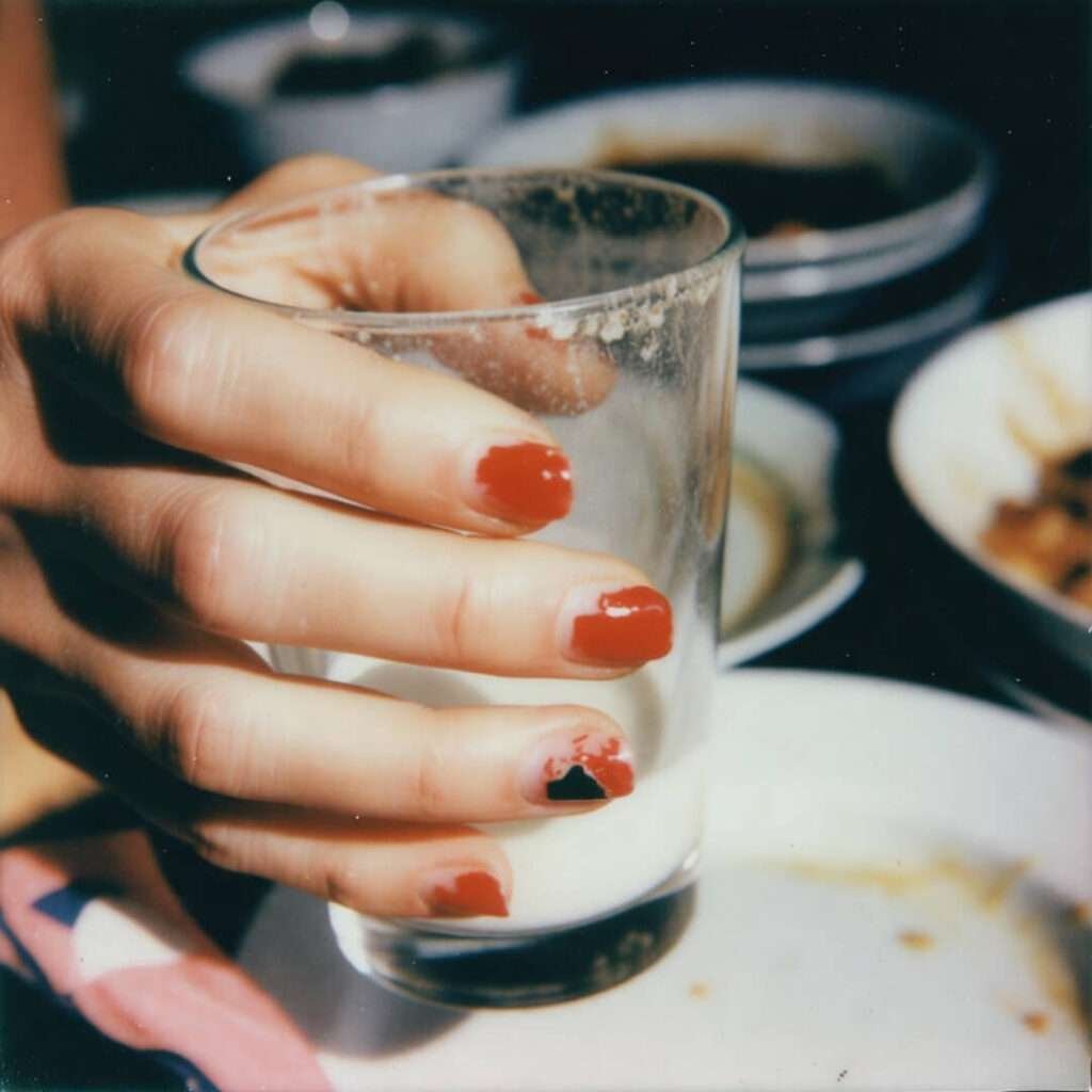 Chipped red nails holding messy mocktail over dirty dishes