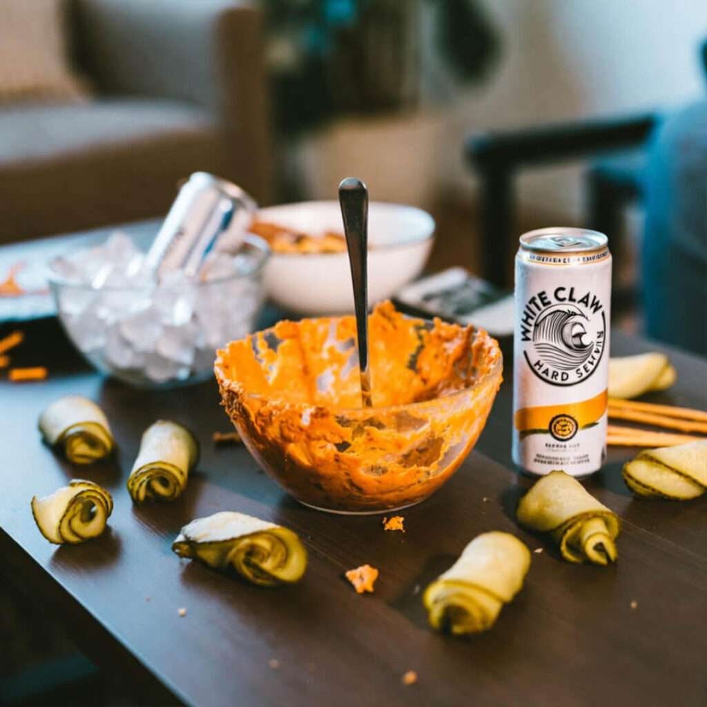 Messy coffee table: half-eaten dip, White Claw, chaos